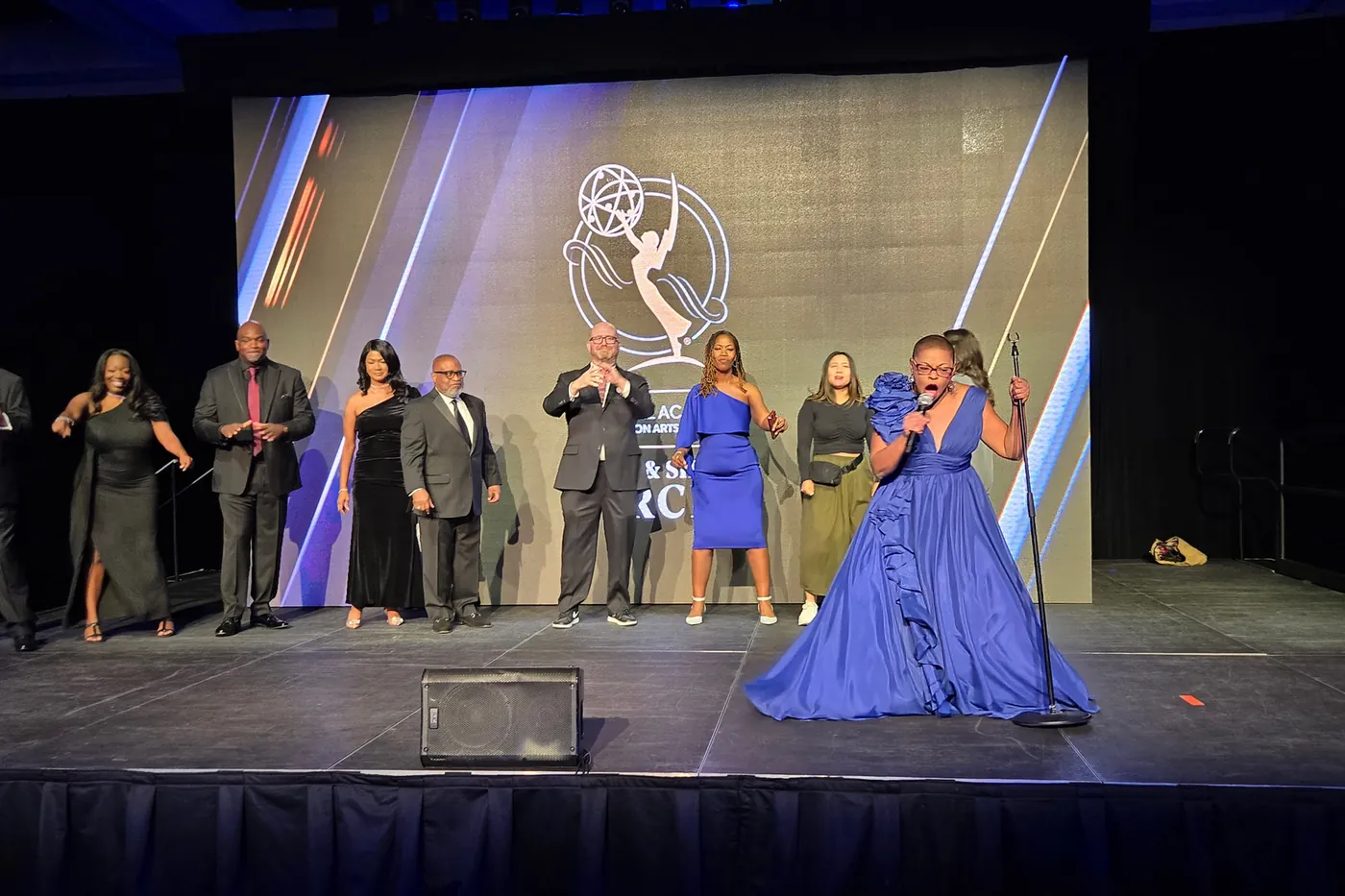 Sheletta Brundidge accepting an Emmy on stage, her production team behind her.