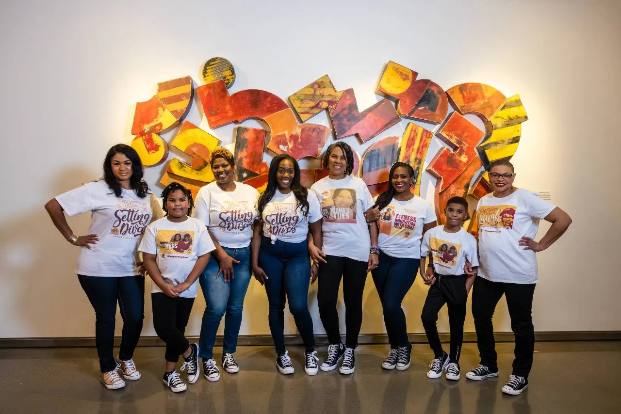 Sheletta and her family in matching ShelettaMakesMeLaugh T-shirts in front of a colorful mural.