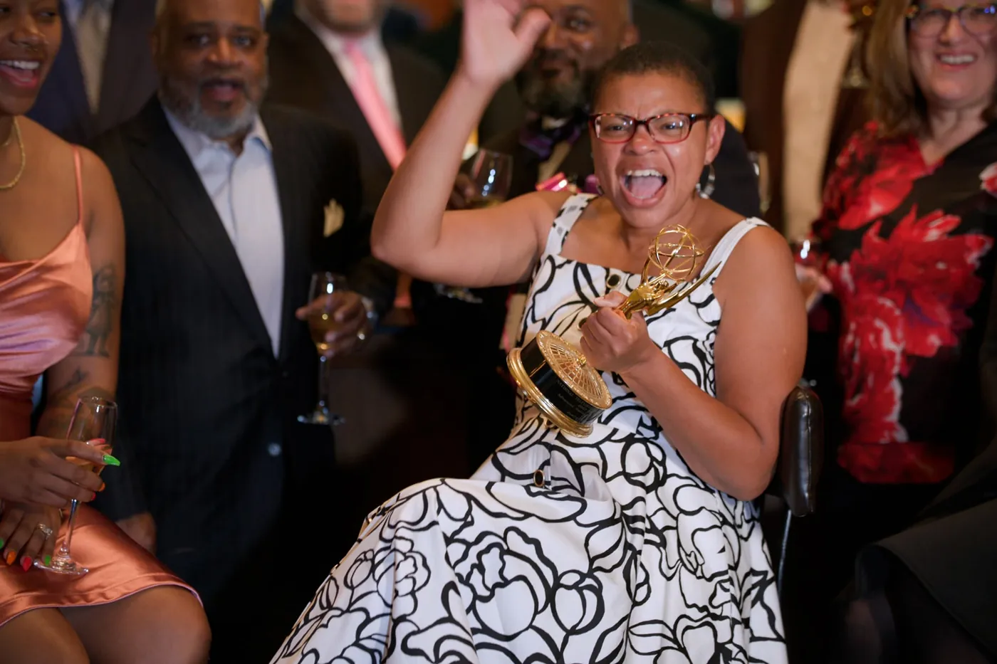 Sheletta Brundidge celebrating with an Emmy statuette, surrounded by cheering friends.
